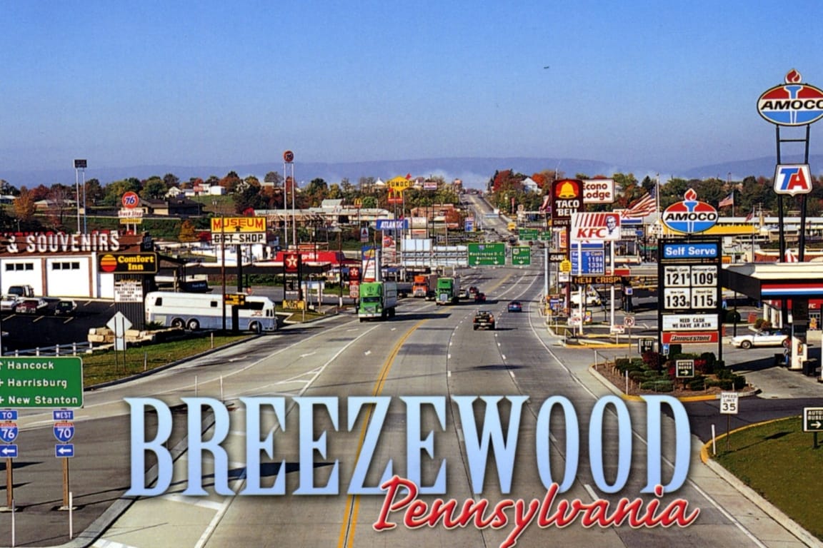 Mock postcard for Breezewood, Pennsylvania, an isometric view fo the main drag on a sunny day, with many car- and truck-oriented chain businesses and wide roads and lanes