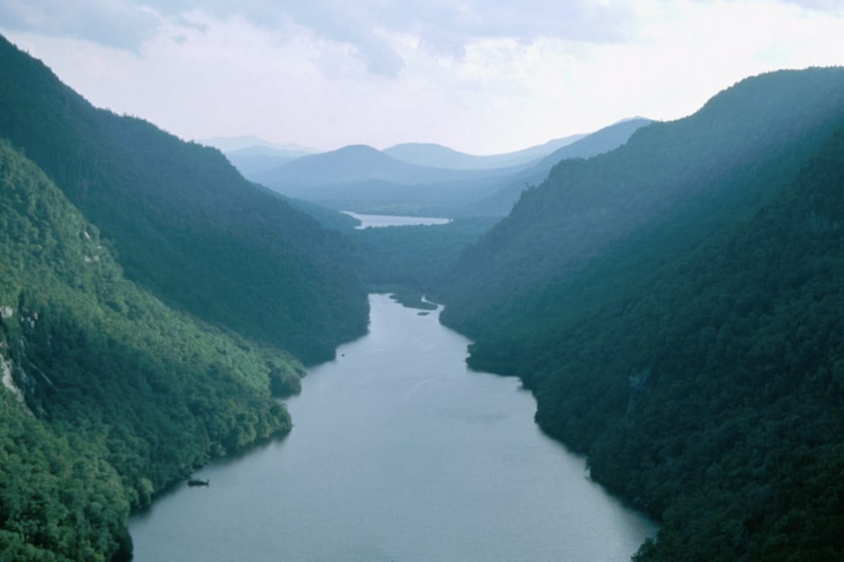 A view along and through a river valley in the thickly forested Adirondack mountains on a partly cloudy day