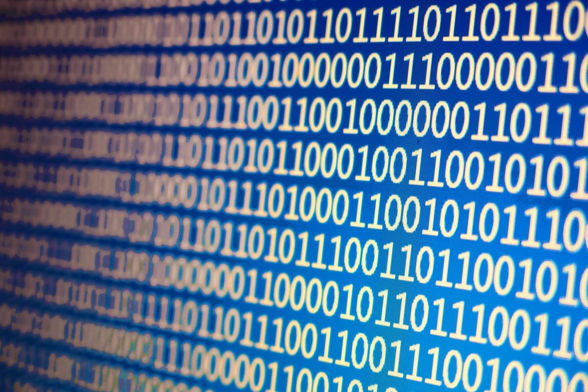 Binary code, ones and zeroes in an off-white font, fills a computer screen with a dark blue background. It is tilted so that the text runs down and towards camera.