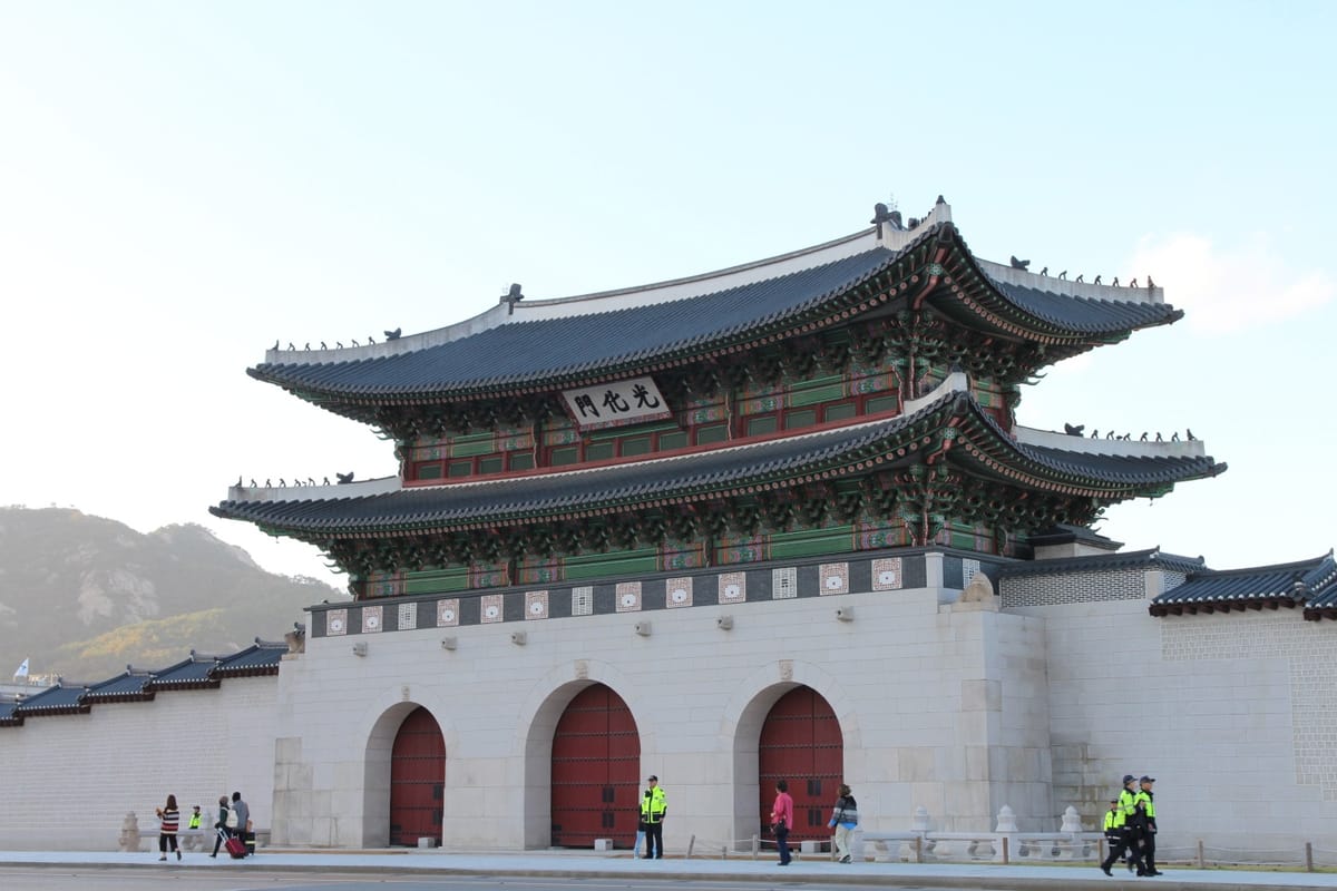 Gwanghwamun, a traditional gate around the old palace in Seoul with cement stone base, closed doors, a wooden pagoda atop, and police officers and civilians in front, in the morning
