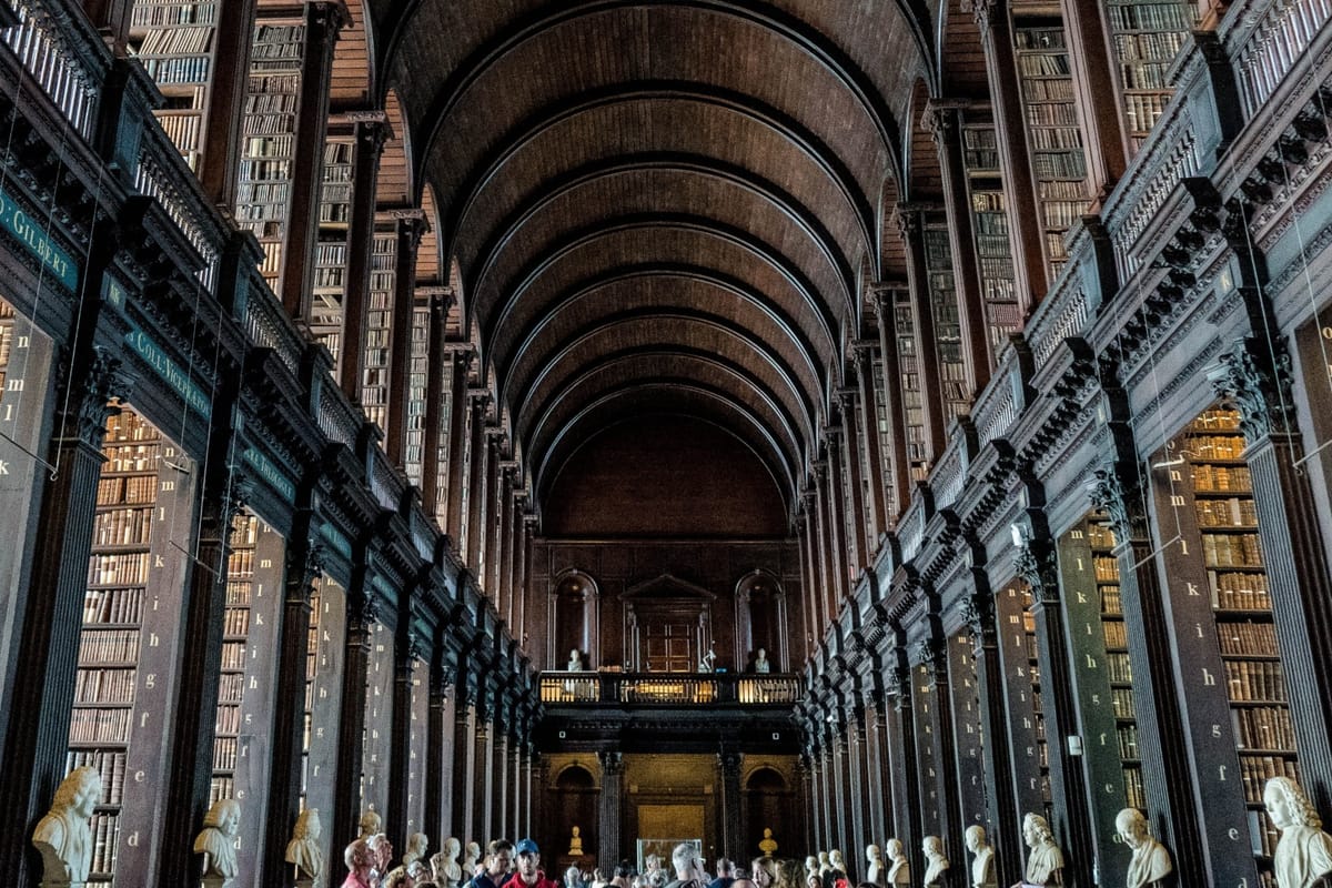 The dark wood interior of a long library, with people in the middle and two floors of books on either side