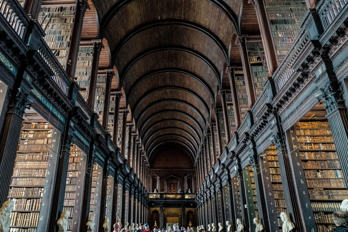 The dark wood interior of a long library, with people in the middle and two floors of books on either side
